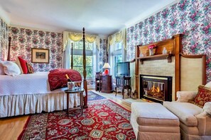 Un dormitorio con cama, chimenea, televisor y ventana con cortinas.