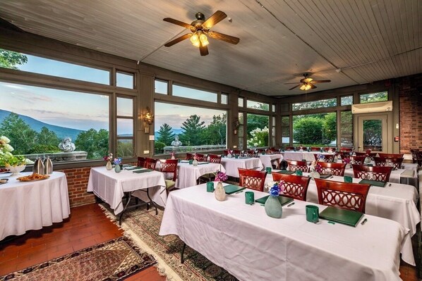 Comedor con mesas listas para el servicio, amplias ventanas con vistas al exterior y ventiladores de techo.