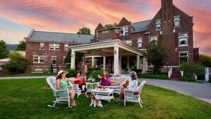Un groupe de personnes est assis à une table sur une pelouse, devant un grand bâtiment en briques doté d’un patio couvert.