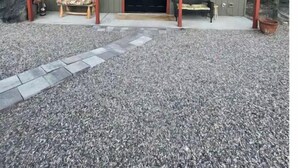 Un bâtiment à l’extérieur d’un vert foncé, avec une porte noire et un petit porche doté de deux bancs en bois.