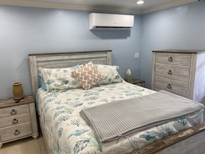 A bedroom with a bed, nightstands, a dresser, and an air conditioning unit.