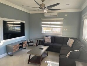 Relax in this stylish living room with a large flat-screen TV, comfortable sofa, and ceiling fan.