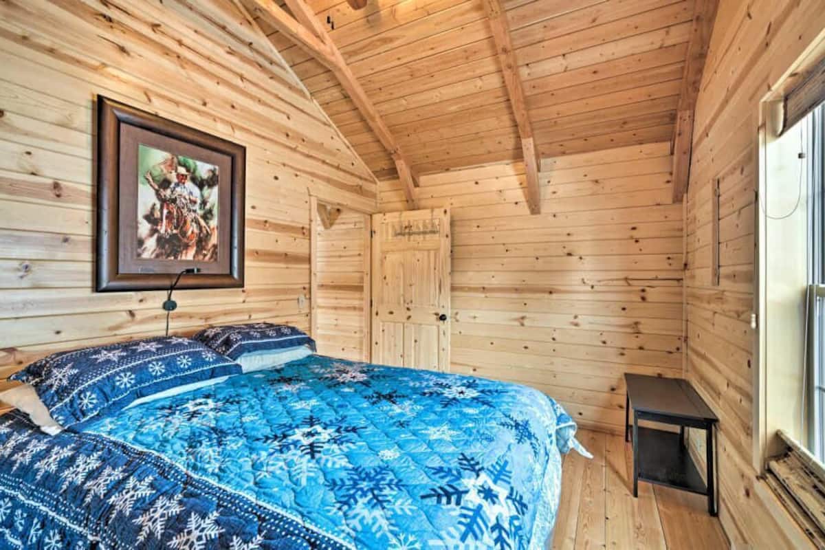 A wooden cabin room with a bed, a framed picture, a door, and a window.