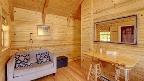 A cozy cabin interior with a wooden ceiling, a sofa with patterned cushions, a small table with stools, and a window with a view. - Rustic Ridge Cabins, Charming Retreat (3 Options!) (Dayton)
