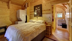 A wooden cabin bedroom with a bed, a white dresser, a painting on the wall, and a small stool. - Rustic Ridge Cabins, Charming Retreat (3 Options!) (Dayton)
