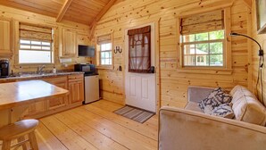A wooden cabin interior with a kitchen, dining area, and a sofa. - Rustic Ridge Cabins, Charming Retreat (3 Options!) (Dayton)