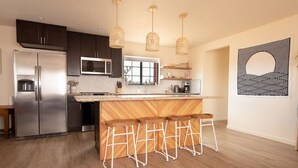 Een moderne keuken met een roestvrijstalen koelkast, een magnetron en een houten kookeiland met barstoelen.