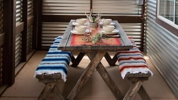 Een rustieke buiten eethoek met een houten tafel en banken, een hanglamp en uitzicht op het woestijnlandschap.