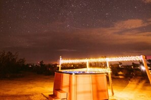 A night scene with a starry sky, a structure with lights, and a sandy ground.