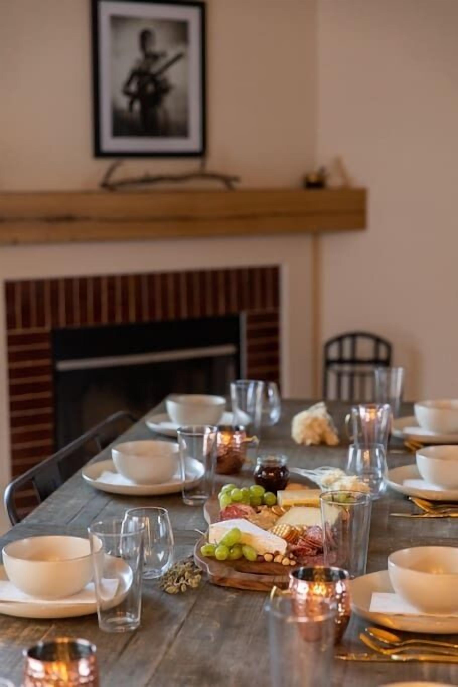 Een eettafel gedekt voor een maaltijd, met borden, glazen en verschillende soorten eten, waaronder kaas en druiven.