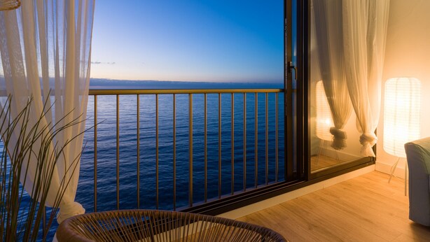Een balkon met uitzicht op zee, een rieten stoel en een lamp.