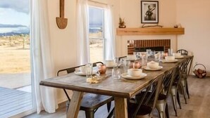 A dining area with a long wooden table set for six, a ceiling fan, and a view of the outdoors.