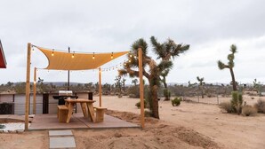 An outdoor patio with a wooden table and chairs, a barbecue grill, and a canopy.