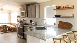 A kitchen with granite countertops, stainless steel appliances, and wooden chairs.