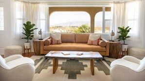 Un salón con un sofá beige, dos mesitas auxiliares, una mesa de centro y vistas a un paisaje desértico a través de amplios ventanales.