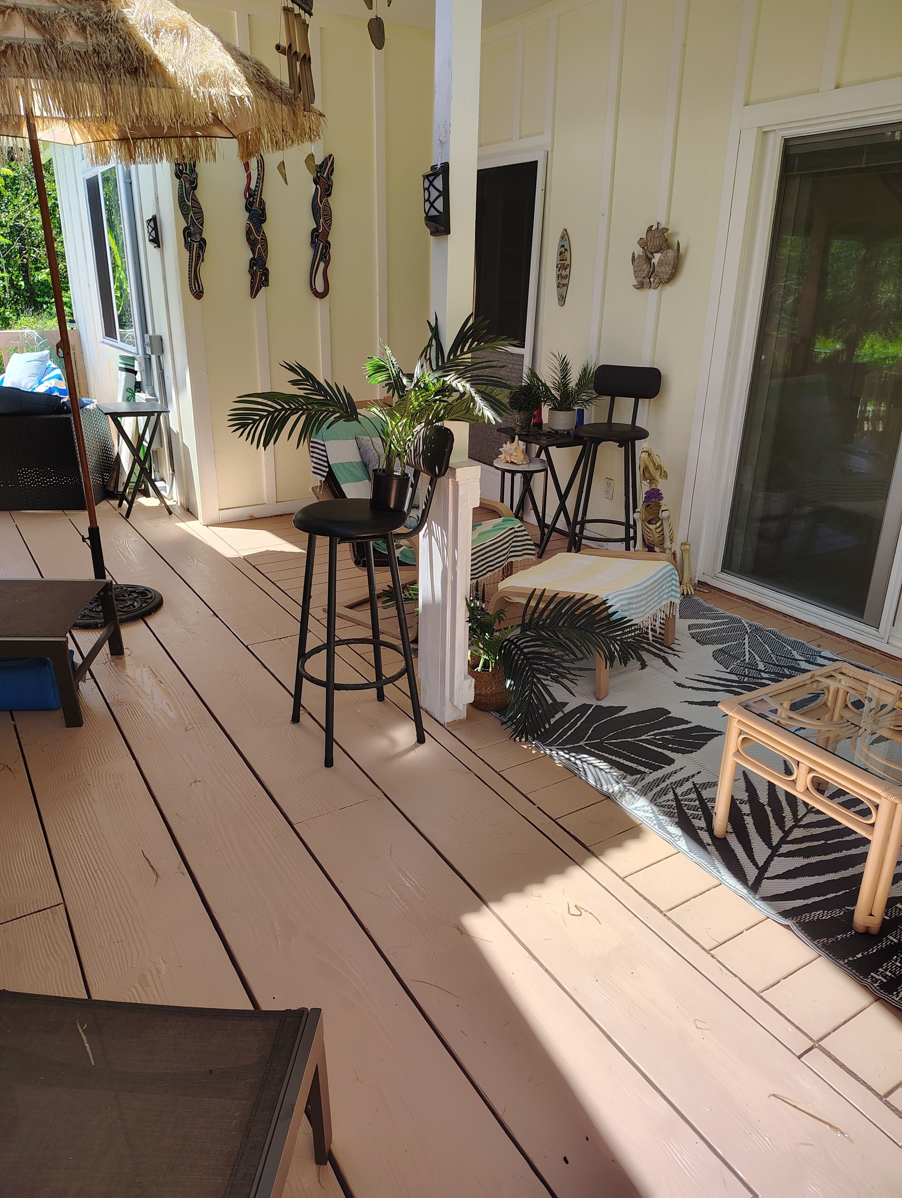 A covered outdoor area with a wooden deck, seating arrangements, and potted plants.
