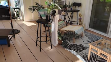A covered outdoor area with a wooden deck, seating arrangements, and potted plants.