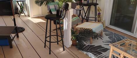 A covered outdoor area with a wooden deck, seating arrangements, and potted plants.