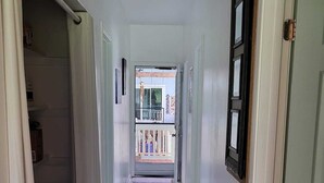 A narrow hallway with a patterned rug, white walls, and a door leading to an outdoor area with a view of a building. - Hoomaikai Blessing's (Keaau)