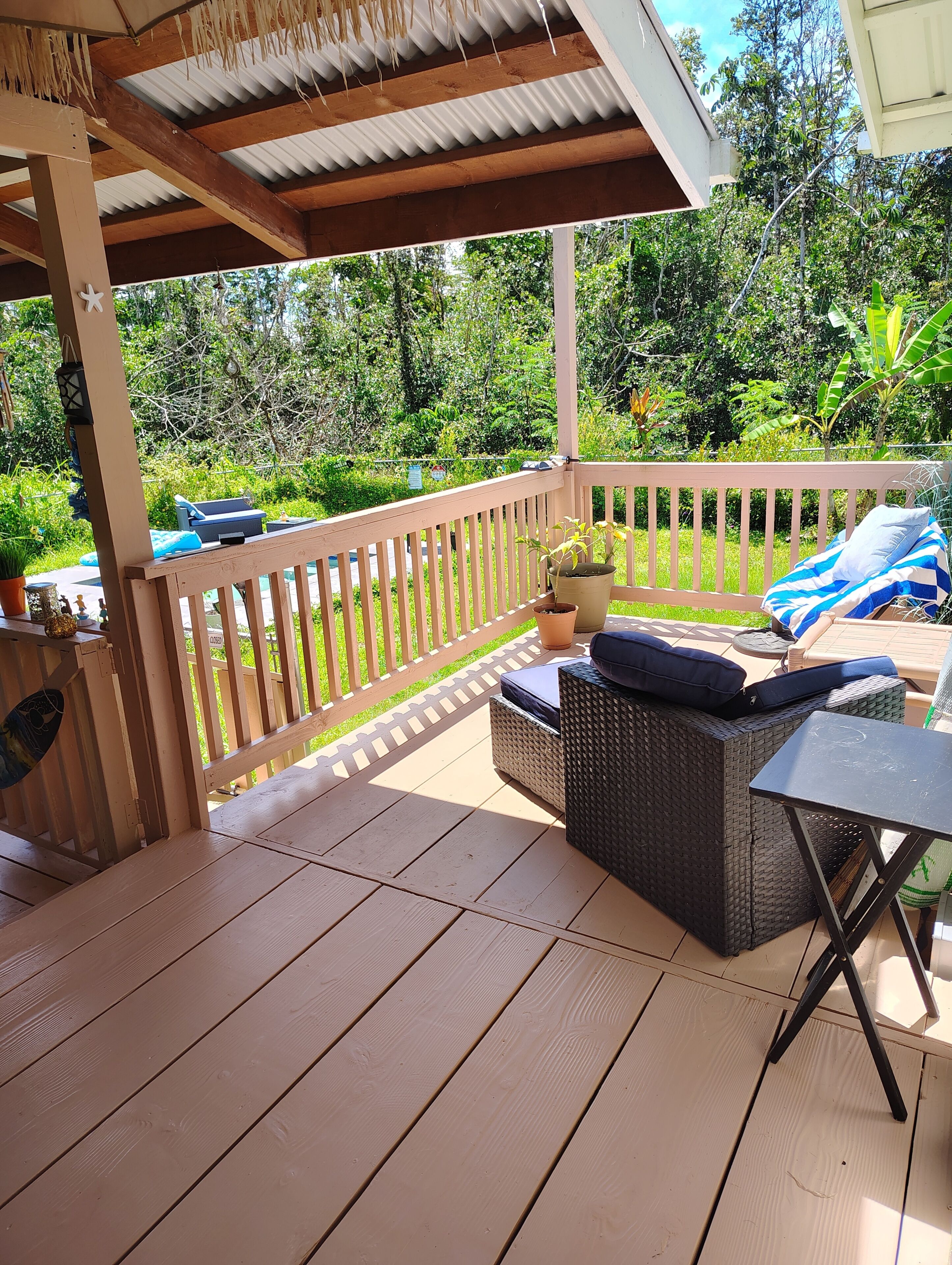 Eine Terrasse im Freien mit Holzfußboden, einem Korbsessel mit Kissen, einem kleinen Tisch und einem Blumentopf.