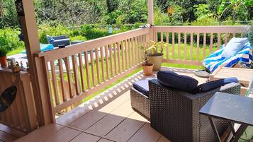 An outdoor deck with a wooden floor, a wicker sofa with cushions, a small table, and a potted plant.