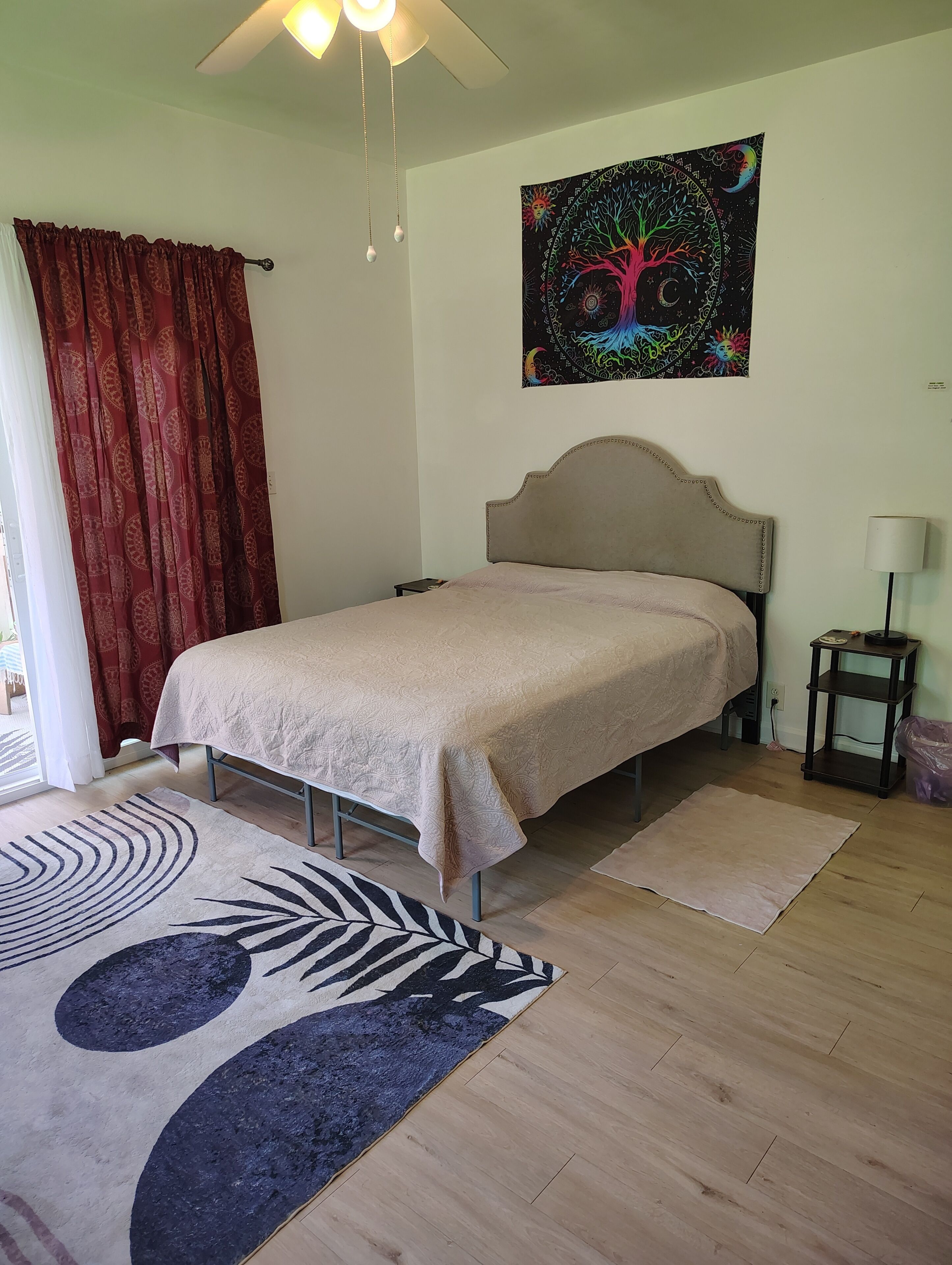 A bedroom with a bed, a ceiling fan, a tapestry, and a nightstand.