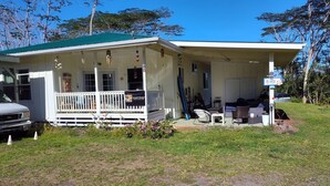 A two-story building with a green roof, a porch with a white railing, and a covered outdoor seating area. - Hoomaikai Blessing's (Keaau)
