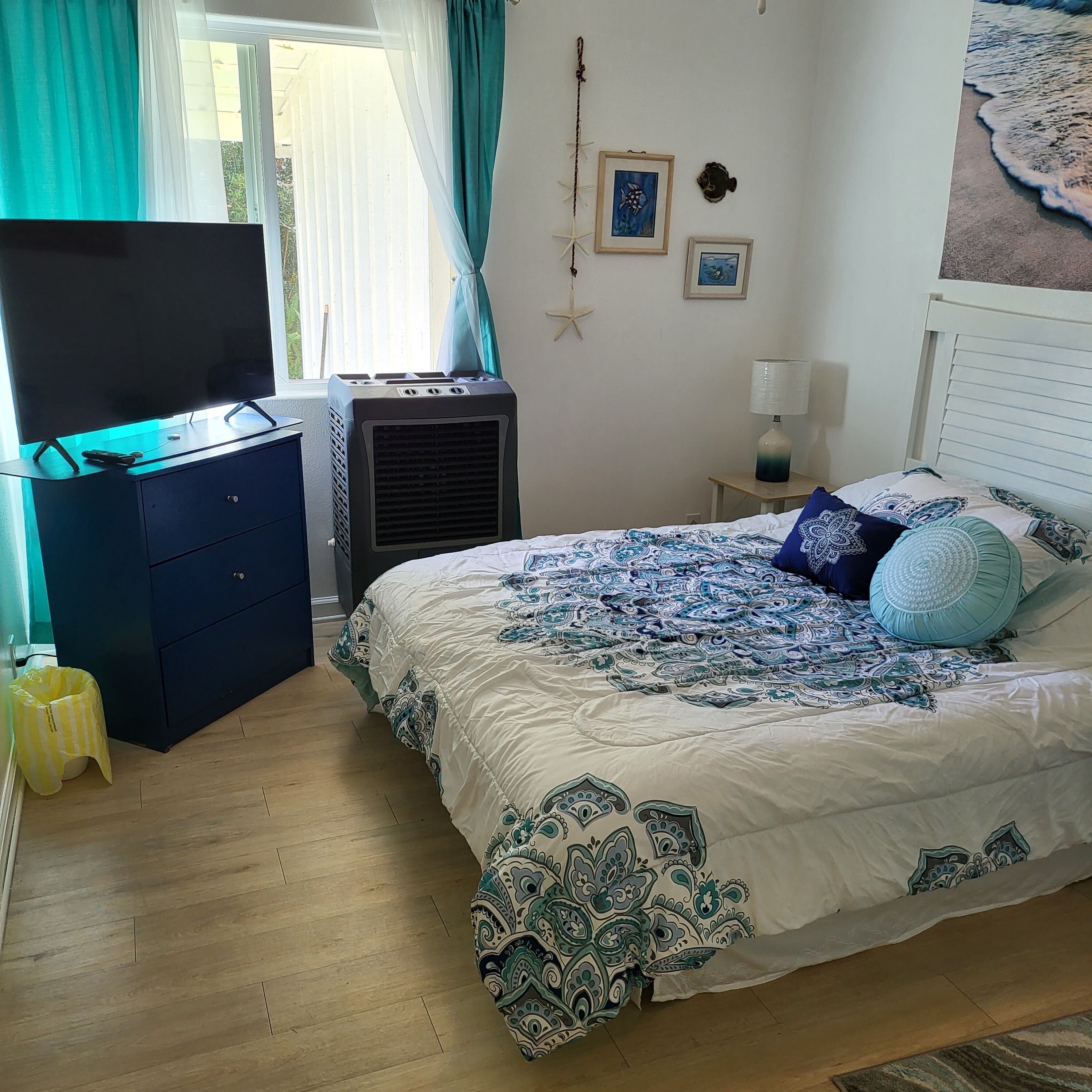 Un dormitorio con una cama, un televisor sobre una cómoda, un calefactor y una ventana con cortinas.