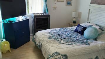 Un dormitorio con una cama, un televisor sobre una cómoda, un calefactor y una ventana con cortinas.