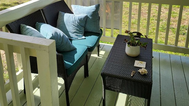 A porch with a wicker sofa and a table, surrounded by a railing, overlooking a garden with a path and greenery. - Hoomaikai Blessing's (Keaau)