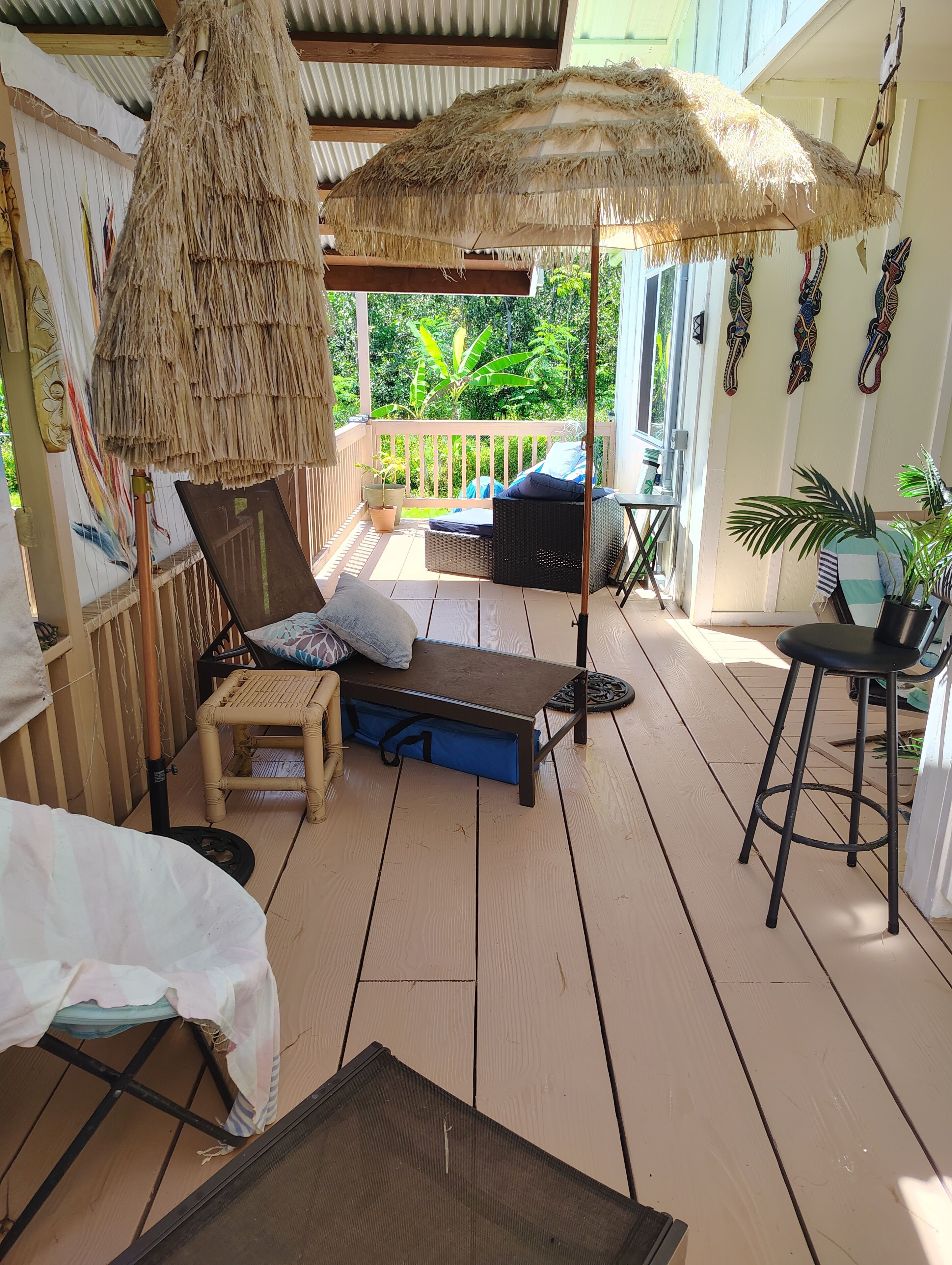 A wooden deck with a thatched umbrella, wicker furniture, and potted plants.