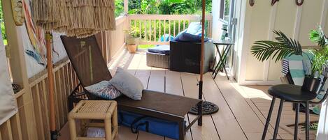 A wooden deck with a thatched umbrella, wicker furniture, and potted plants.