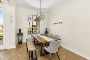A dining area with a wooden table, benches, and a chandelier. - Orange Oasis - A Private Tropical Paradise (Cape Coral)