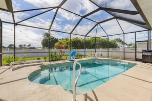 A covered swimming pool with a metal frame, surrounded by a white fence, and a grill area to the right. - Orange Oasis - A Private Tropical Paradise (Cape Coral)