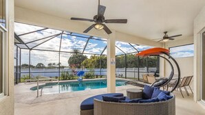 Un espace extérieur abrité doté d’une piscine, de meubles en osier, de ventilateurs de plafond et offrant une vue sur le paysage environnant.
