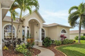 Step into a serene oasis with a covered porch surrounded by lush tropical plants and a beautifully manicured lawn.