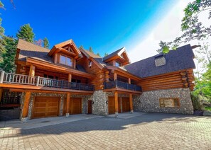 A large log cabin with multiple balconies, stone foundations, and a spacious front porch. - Grand Alpine Lodge, Ski In/Out, Hot Tub, Sleeps 20 (Whitefish)