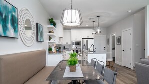 A modern kitchen with white cabinets, a central island, and a dining area with a table and chairs. - 3 Bedroom Townhome in the heart of downtown Gilbert, AZ - Lot 30 (Gilbert)