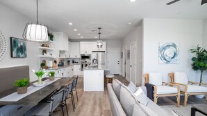 A modern kitchen with white cabinets, a central island, and a dining area with a long table and chairs. - 3 Bedroom Townhome in the heart of downtown Gilbert, AZ - Lot 30 (Gilbert)