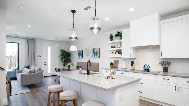 A modern kitchen with white cabinets, a central island with stools, pendant lighting, and a view to the living area. - 3 Bedroom Townhome in the heart of downtown Gilbert, AZ - Lot 30 (Gilbert)