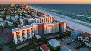 Ein Hotel an der Küste mit mehreren Gebäuden, einem Strand und einem Tennisplatz.