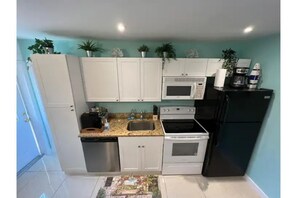 Compact kitchen with white cabinetry, granite countertop, microwave, oven, and dishwasher.
