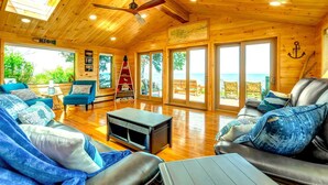 Una cabaña de madera espaciosa con techo alto, ventanas grandes y vista al mar.