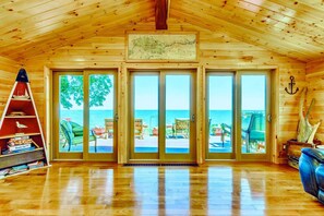 A wooden cabin with a large sliding glass door leading to a deck with outdoor seating and a view of the ocean.