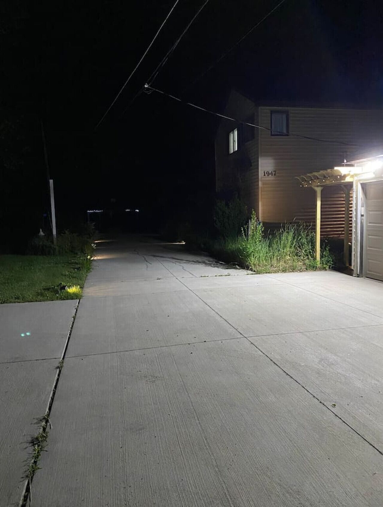 A residential driveway at night with a house number 1947, a garage, and a well-lit entrance.