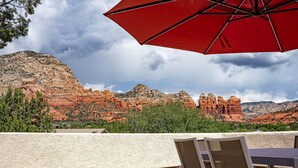 A terrace with a red umbrella, white chairs, and a view of red rock formations. - Modern Sedona Escape Rooftop Views, Trails Nearby, Pet Friendly (Sedona)