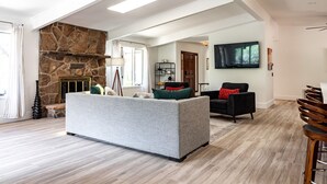 A spacious living room with a stone fireplace, a grey sofa, a black armchair, and a TV mounted on the wall. - Modern Sedona Escape Rooftop Views, Trails Nearby, Pet Friendly (Sedona)