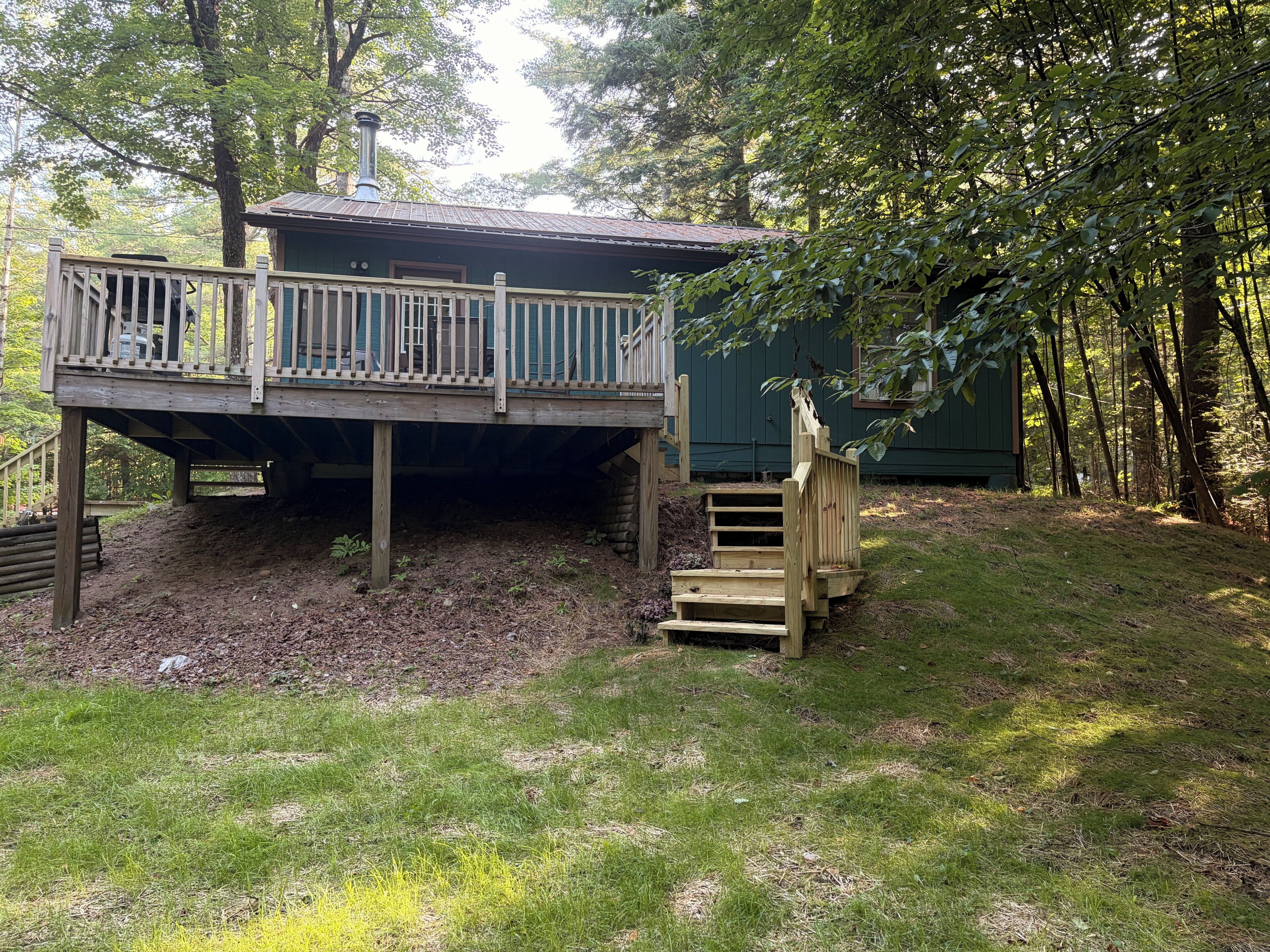 Une terrasse en bois avec une rambarde, un escalier menant à un bâtiment, et une zone boisée en arrière-plan.