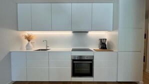 Une cuisine moderne avec des meubles blancs, un four encastré et une machine à café posée sur le plan de travail.