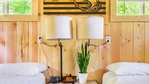 Een kamer met houten lambrisering, twee bedden, een digitale klok, twee wandlampen en een potplant.